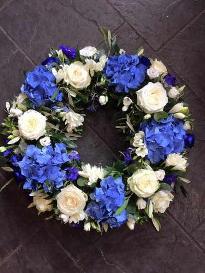 Wreath SYM-316 - A beautiful classic wreath arranged using purple and white flowers and finished with fine foliage.
